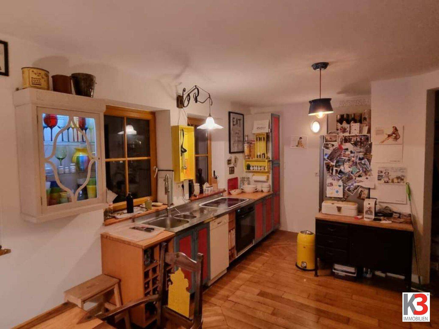 Bunte Küche mit Holzfußboden, Spüle und verschiedenen Schränken, die eine lebendige Atmosphäre schaffen.