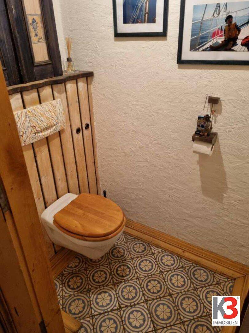 Separates WC mit Holzverkleidung, Toilette mit Holzdeckel und gemustertem Fliesenboden.