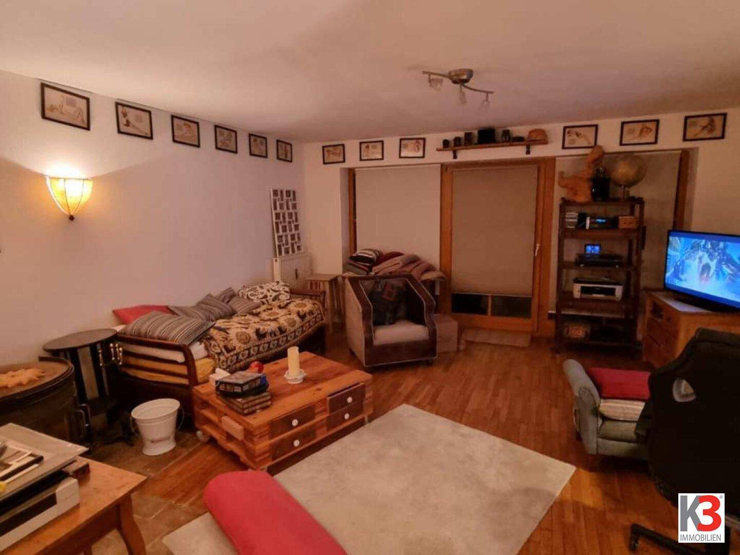 Geräumiges Wohnzimmer mit Zugang zu einem Außenbereich, Fernseher und gemütlichen Sitzgelegenheiten.