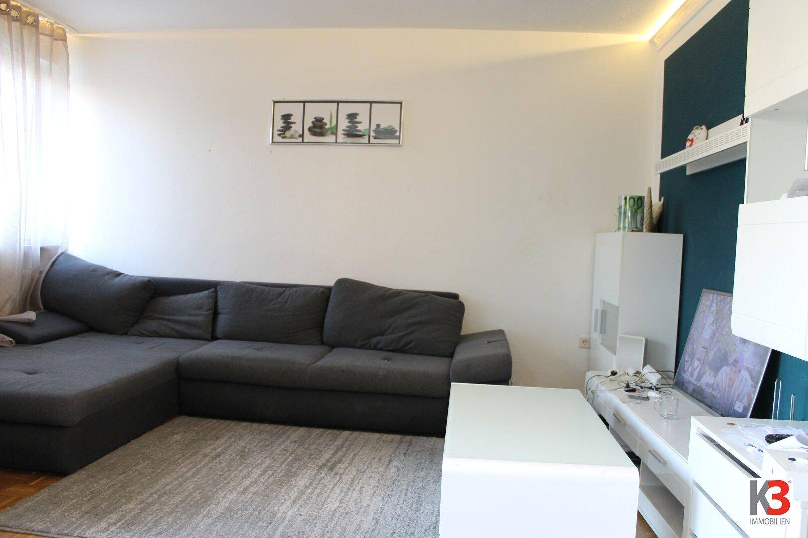 Gemütliches Wohnzimmer mit großem Ecksofa, hellem Teppich und einer farbigen Akzentwand.