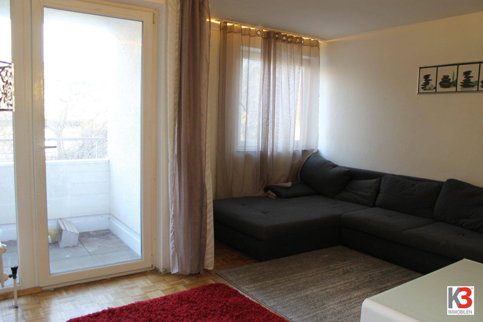 Helles Wohnzimmer mit Zugang zu einem kleinen Balkon, ausgestattet mit einem bequemen Ecksofa.