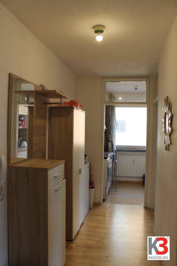 Heller Flur mit Holzmöbeln, Spiegel und Blick in einen angrenzenden Raum mit Fenster.