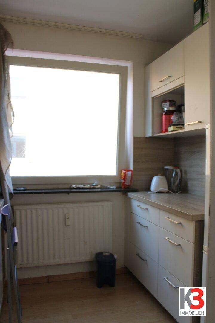 Helle Küchenzeile mit weißen Unterschränken, Holz-Arbeitsplatte und großem Fenster.