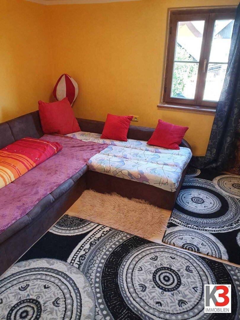Gemütliches Schlafzimmer mit gelben Wänden, Ecksofa und gemusterten Teppichen.