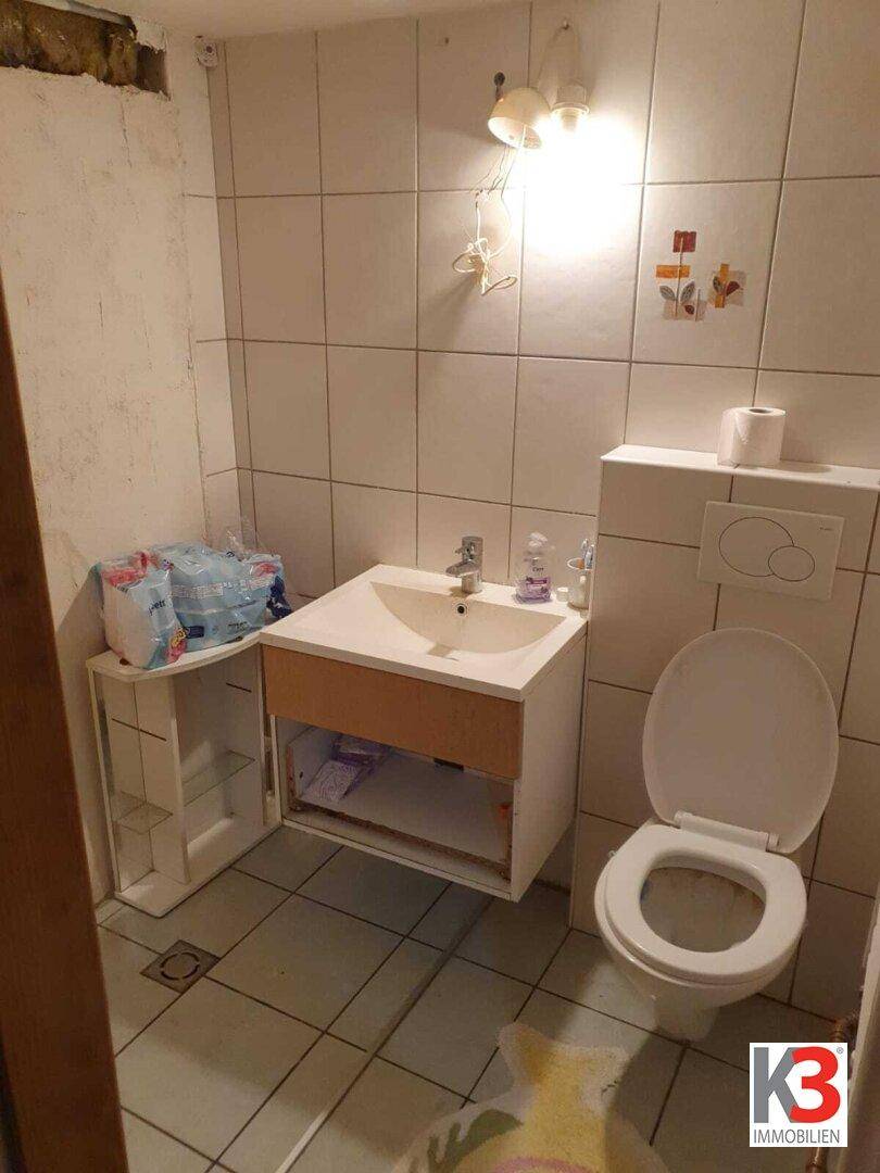 Einfaches WC mit weißen Fliesen, Toilette und Waschbecken.