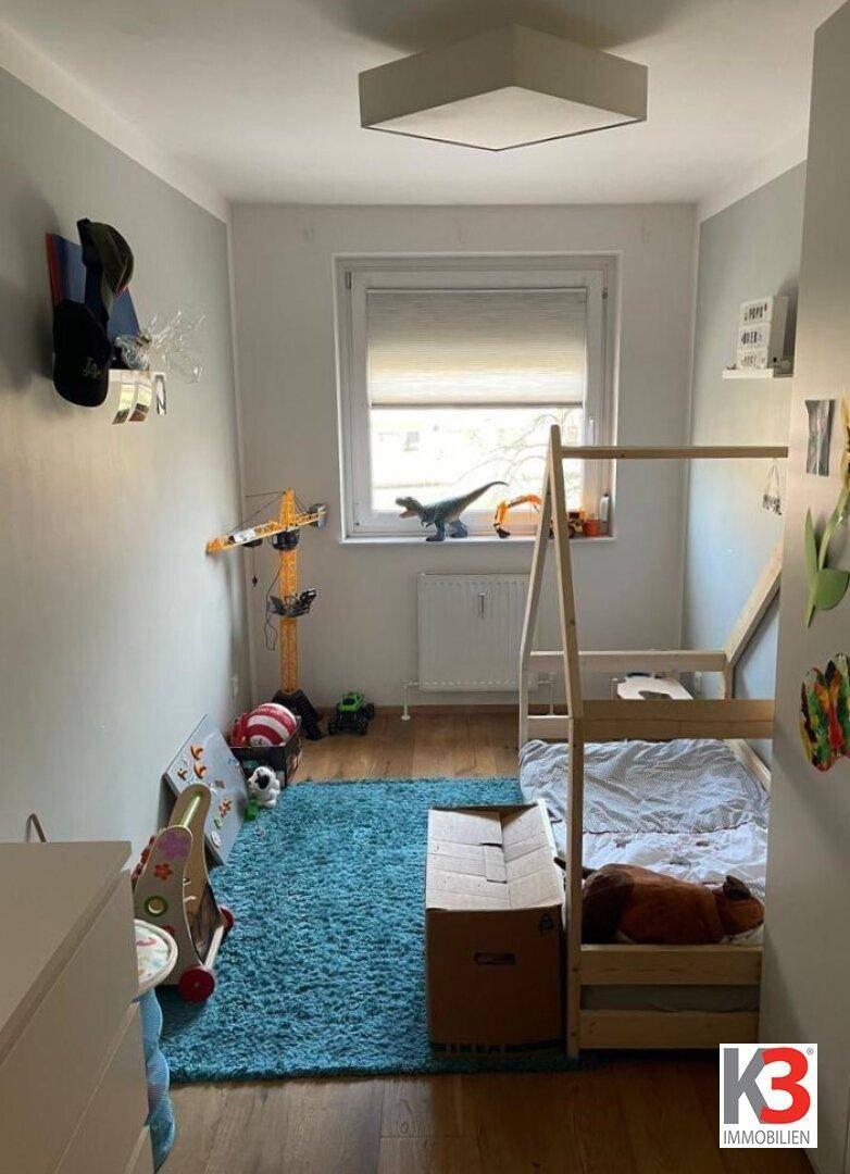 Kinderzimmer mit Holzboden, blauem Teppich und einem kleinen Bett.