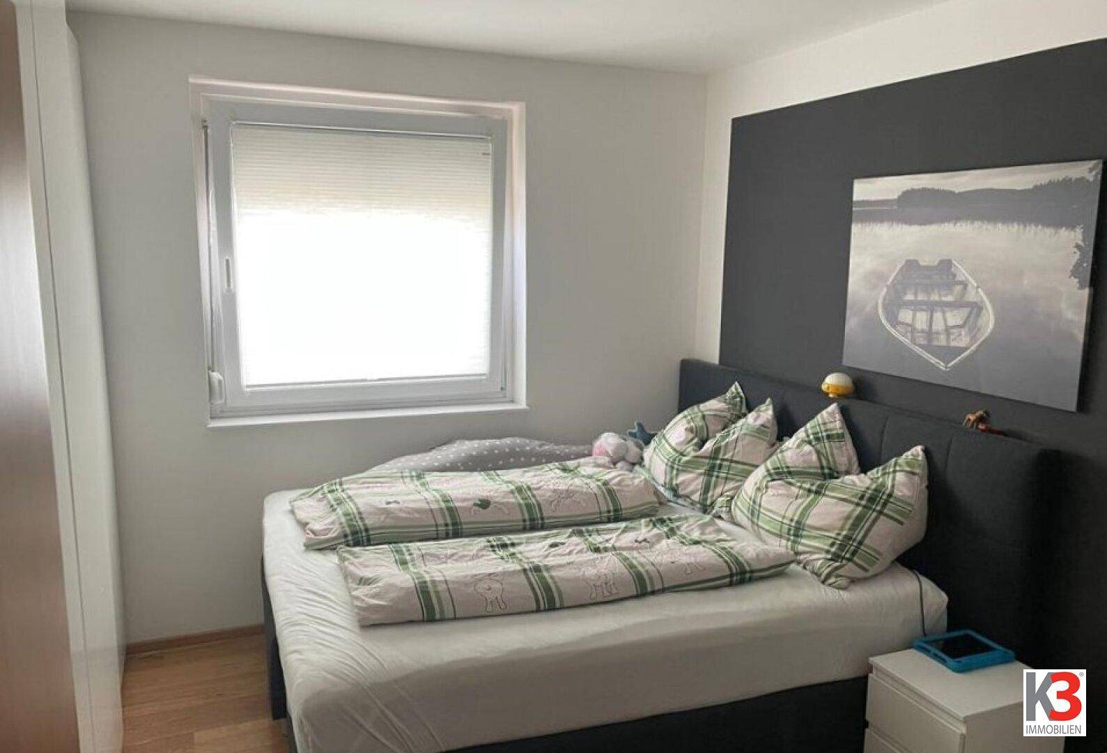 Schlafzimmer mit Doppelbett, karierter Bettwäsche und dunkler Akzentwand.