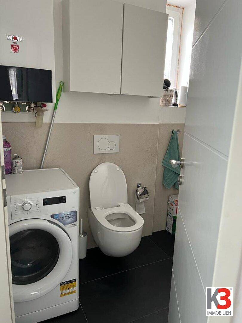 Kleines WC mit Toilette, Waschmaschine und Wandregalen.