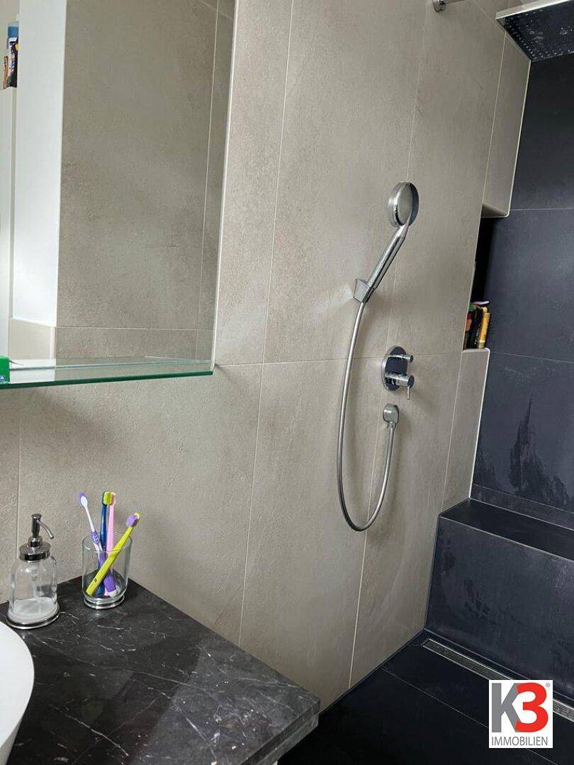 Duschbereich im Badezimmer mit Handbrause und dunklen Fliesen.