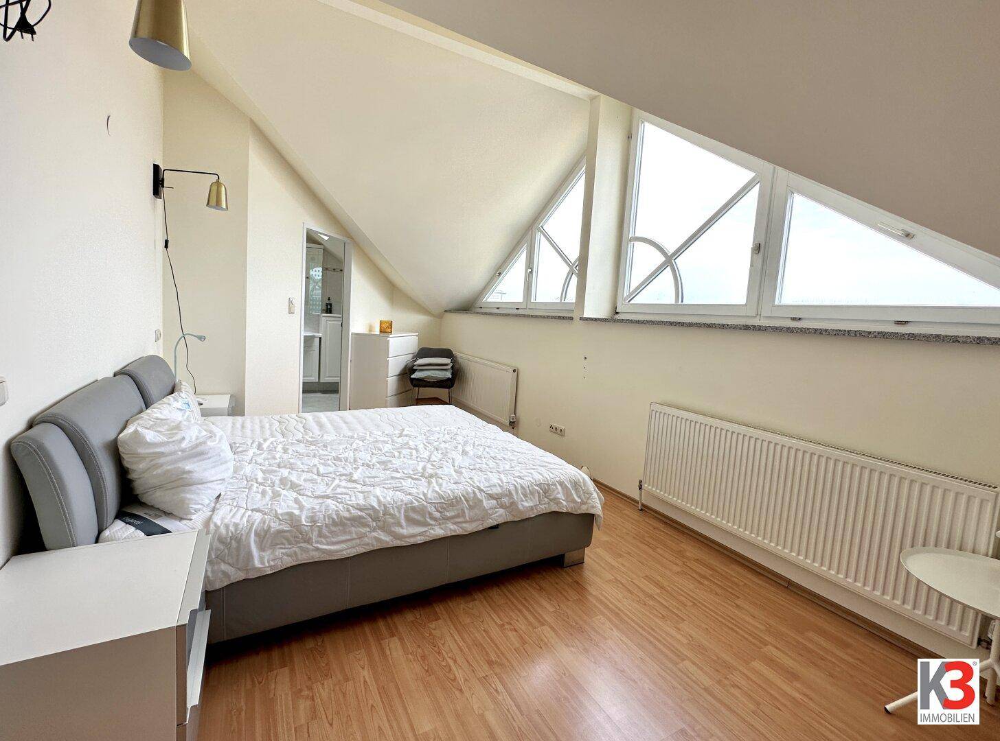 Schlafzimmer mit Doppelbett, Dachschrägen und großen Fenstern für viel Tageslicht.
