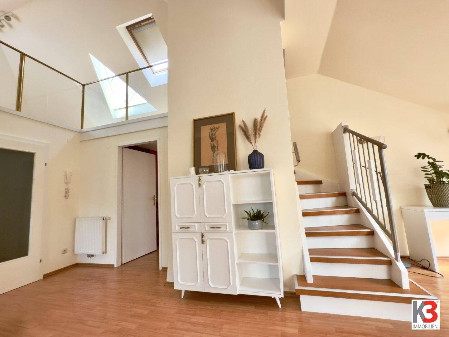 Eingangsbereich mit Treppe zur oberen Etage, Holzboden und einem dekorativen Schrank.