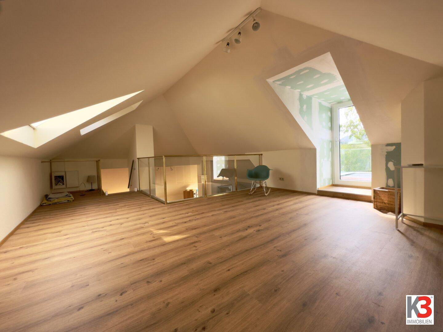 Großer offener Dachbodenraum mit Holzboden, Dachschrägen und einem großen Fensterbereich.