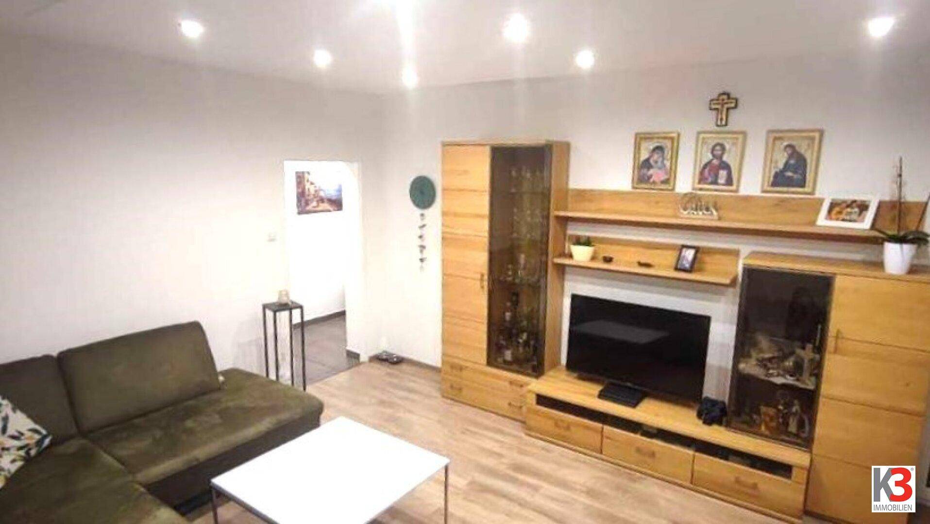 Gemütliches Wohnzimmer mit grünem Ecksofa, Holz-Wohnwand und hellem Holzboden.