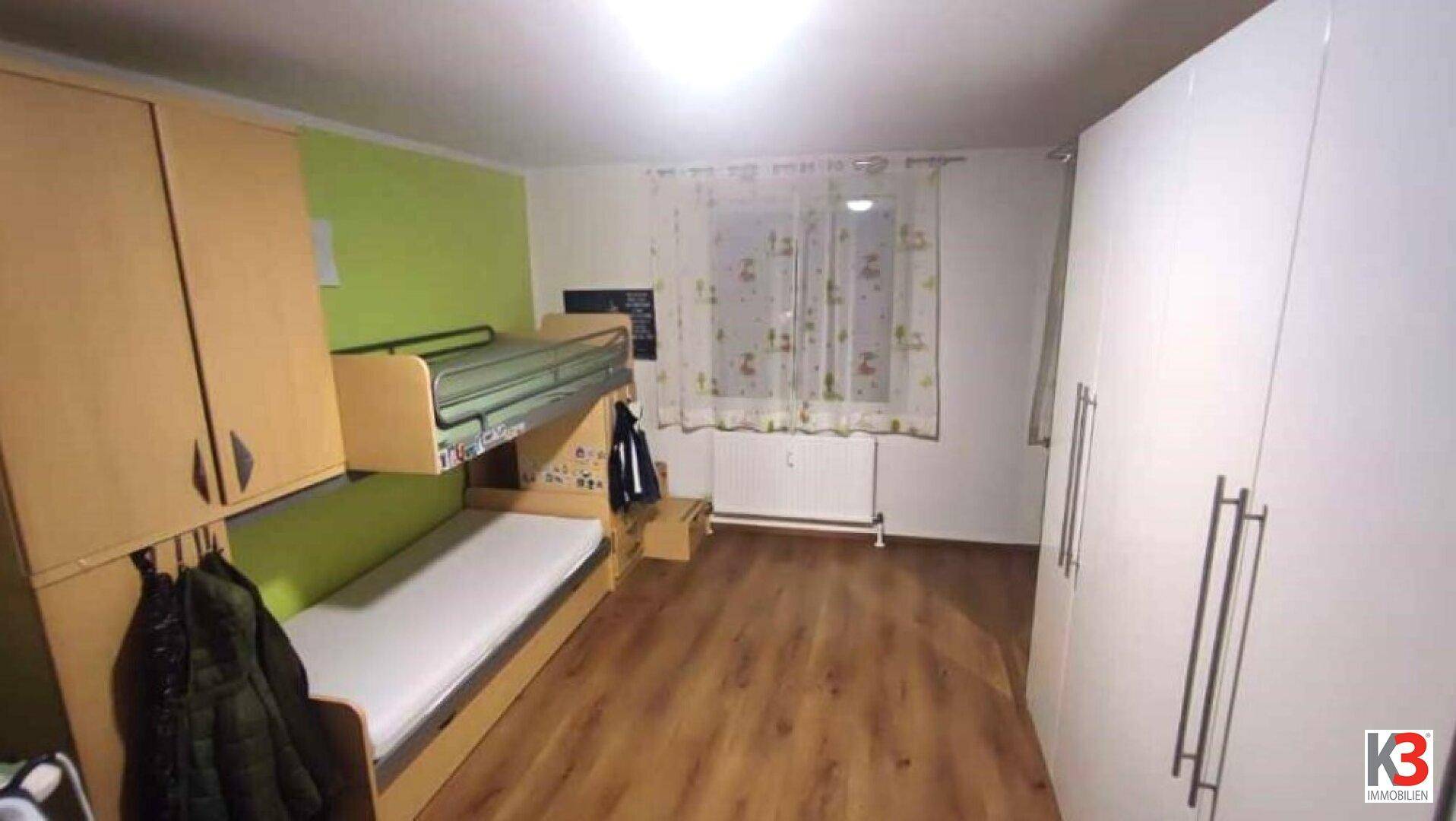 Kinderzimmer mit Etagenbett, grün akzentuierter Wand und geräumigen weißen Kleiderschränken.
