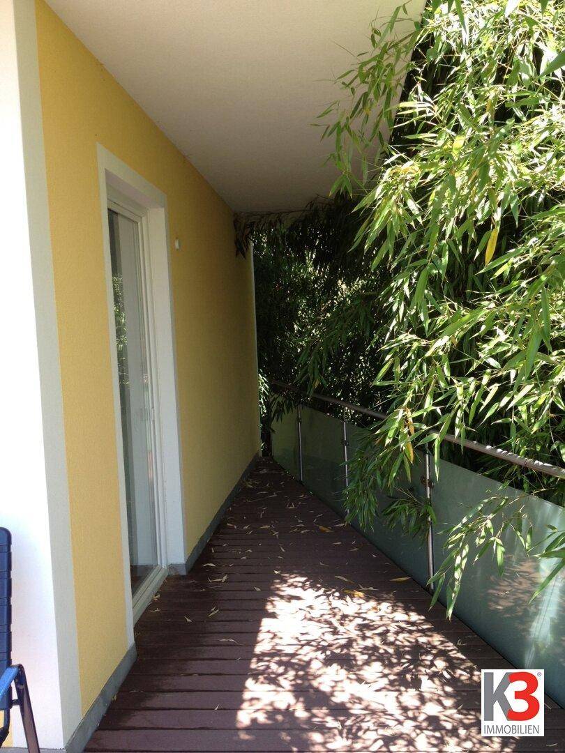 Schmaler, überdachter Balkon mit Holzboden und üppigem Bambusbewuchs, der Privatsphäre bietet.