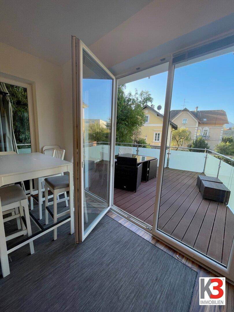 Essbereich mit Bartisch und Stühlen, der sich zu einer sonnigen Terrasse öffnet und viel Licht hereinlässt.
