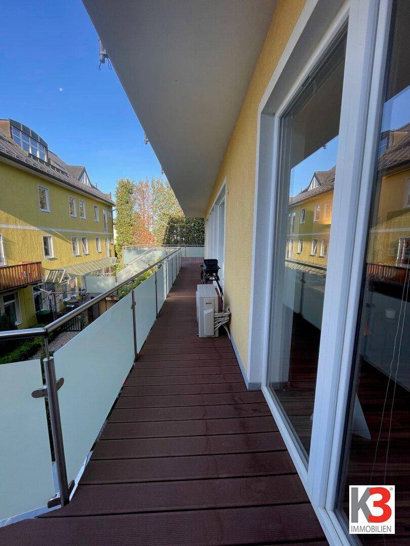 Langer Balkon mit Holzboden und Blick auf die umliegenden Gebäude unter blauem Himmel.