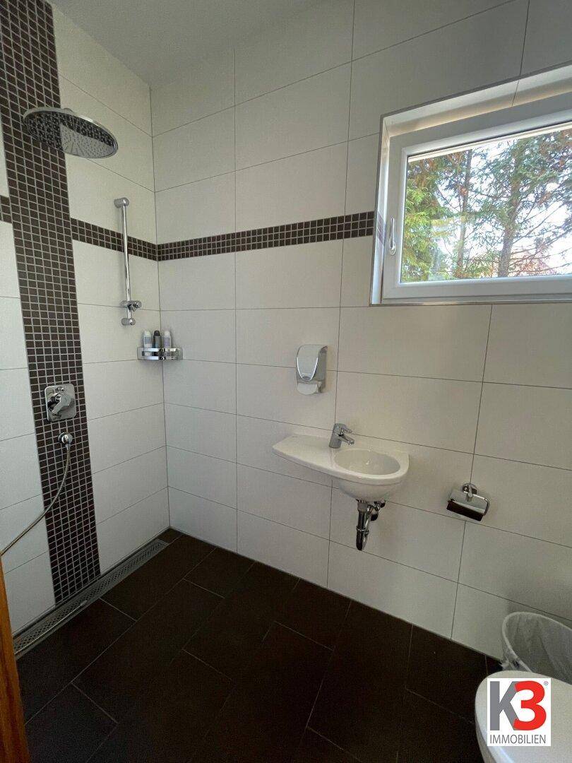 Modernes Badezimmer mit ebenerdiger Dusche, kleinem Waschbecken und Fenster für Tageslicht.