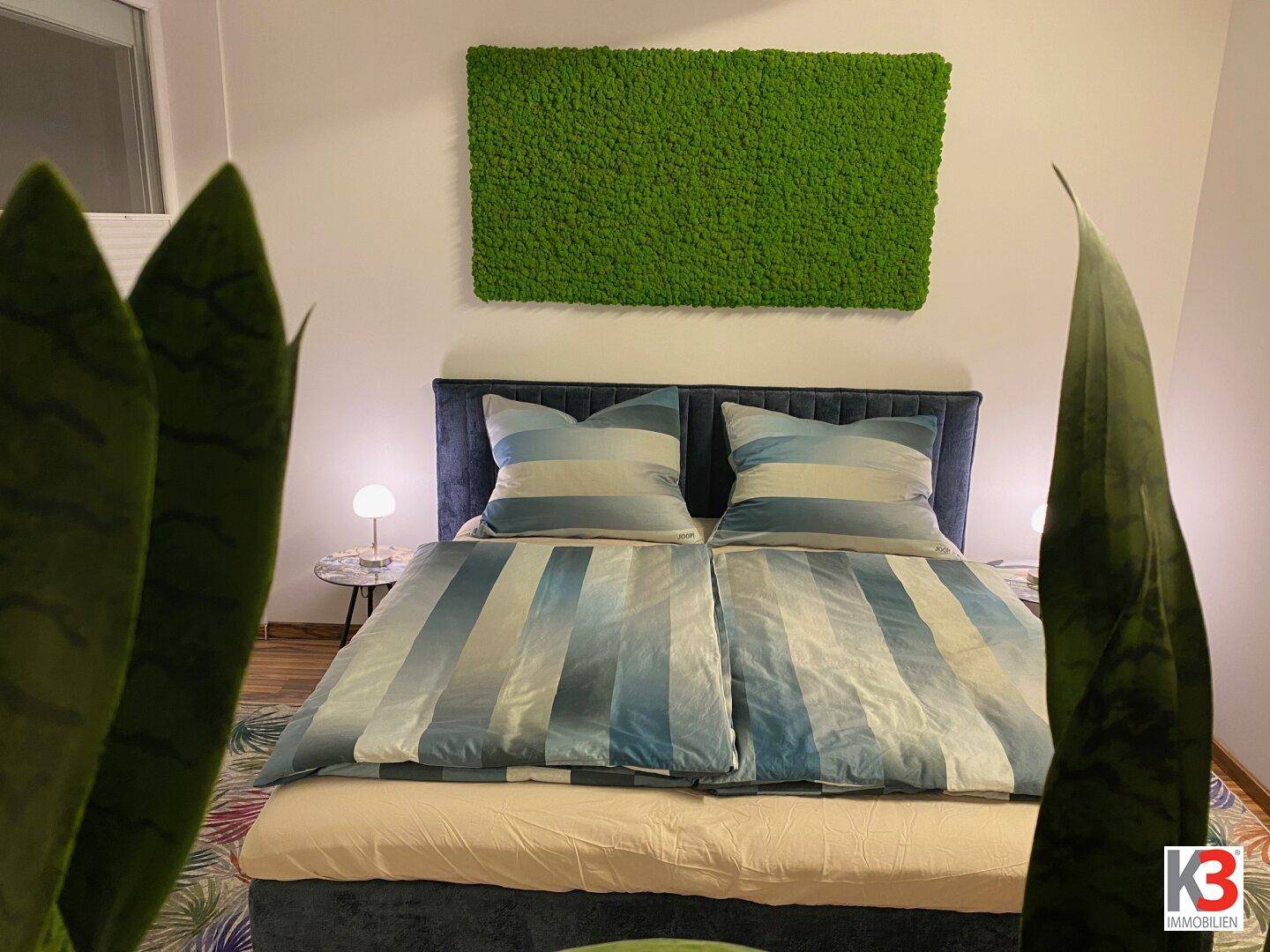 Gemütliches Schlafzimmer mit Doppelbett, dekorativer Mooswand und Zimmerpflanze.