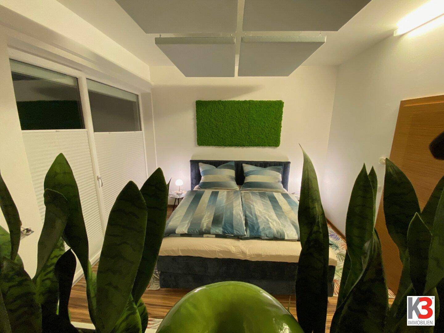Schlafzimmer mit großem Bett, Holzboden und Fenster, das viel Tageslicht hereinlässt und eine helle Atmosphäre schafft.