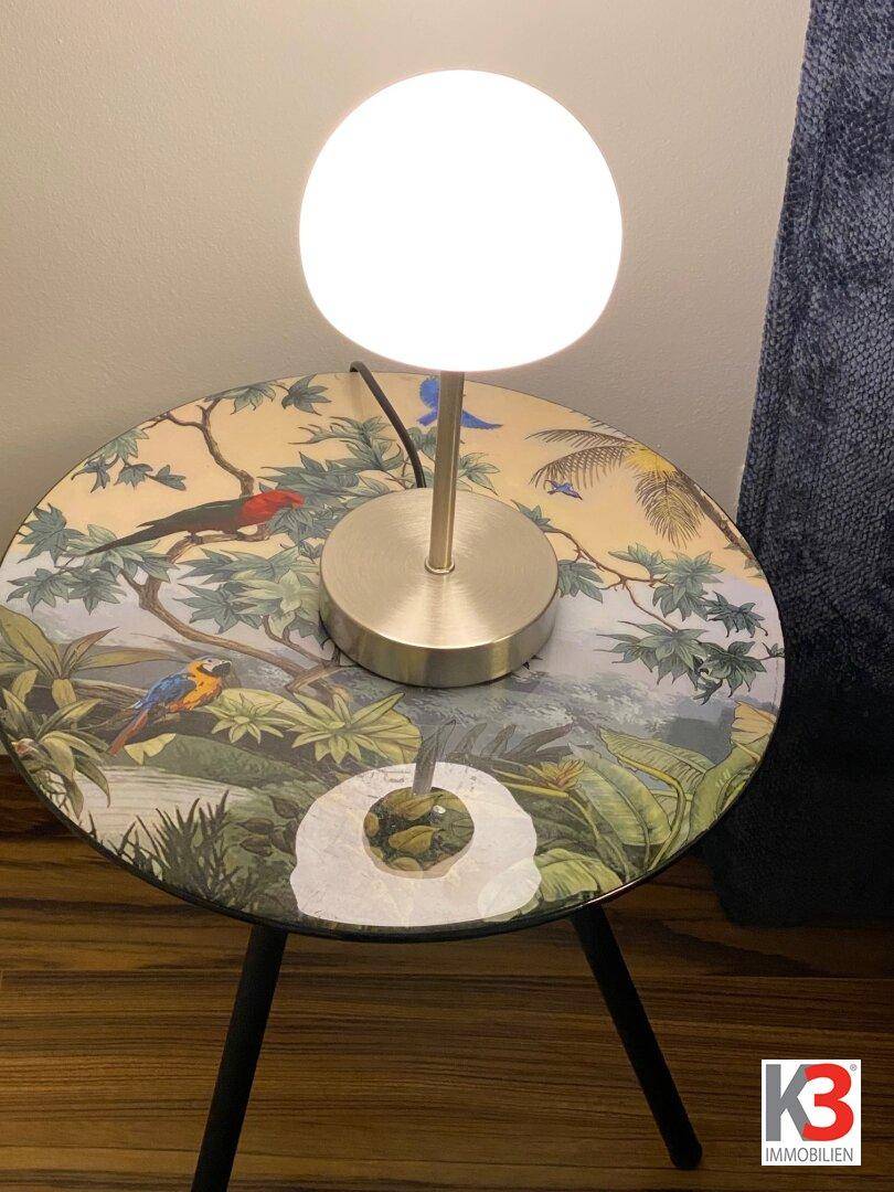 Nahaufnahme eines runden Beistelltisches mit Lampe und farbenfrohem tropischen Dekor.