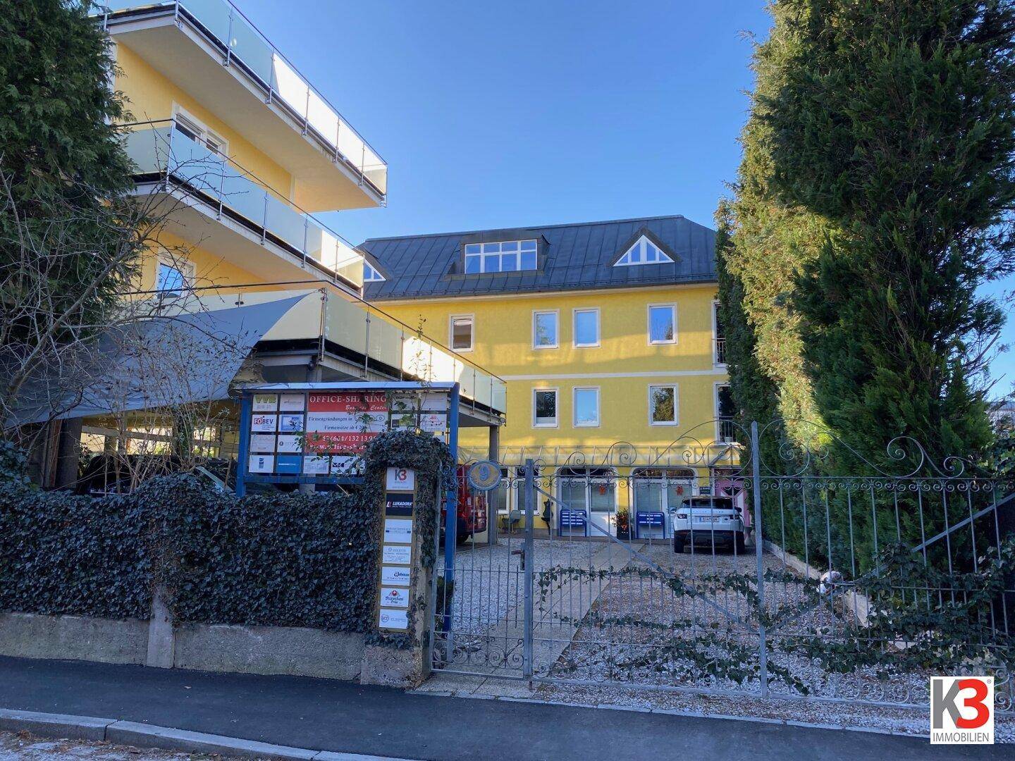 Gelbes Mehrfamilienhaus mit mehreren Etagen und Balkonen, umgeben von Grünflächen.