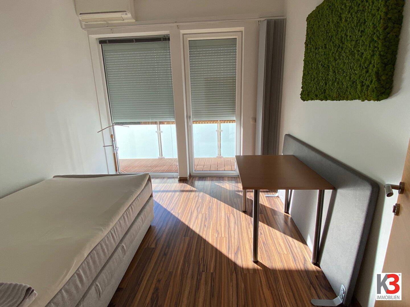 Schlafzimmer mit Einzelbett und Schreibtisch, mit Zugang zu einem Balkon.