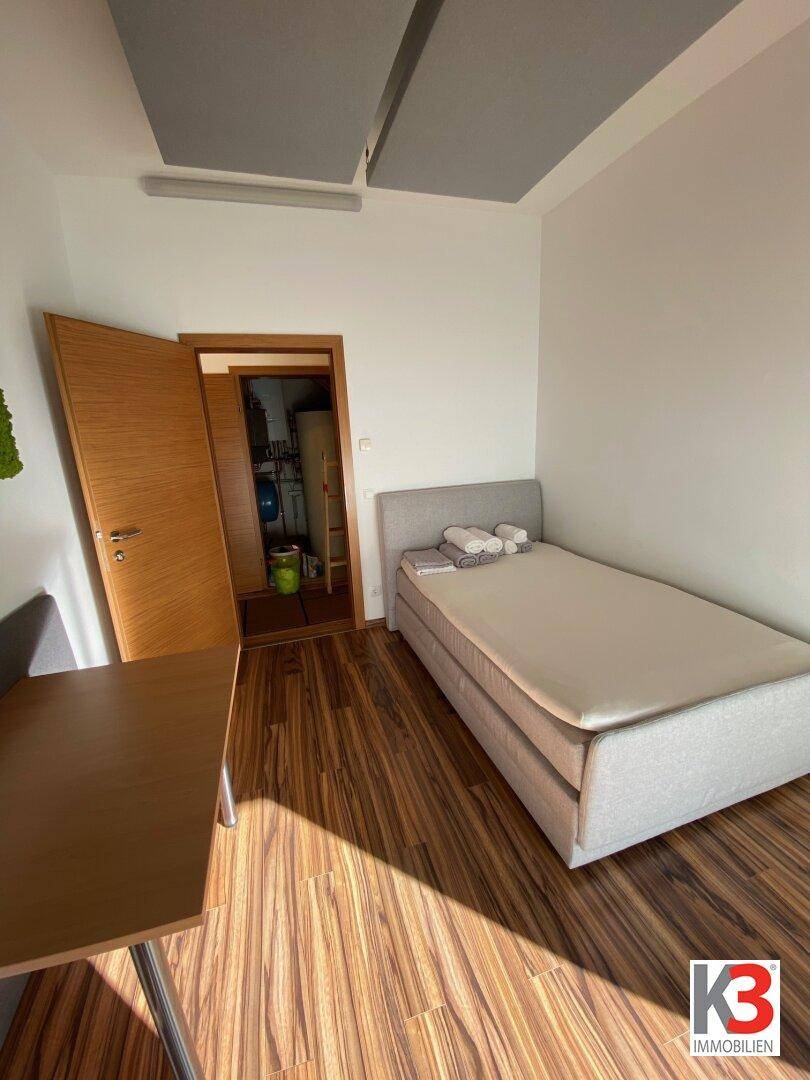 Schlafzimmer mit Einzelbett und Schreibtisch, angrenzend an einen praktischen Abstellraum.