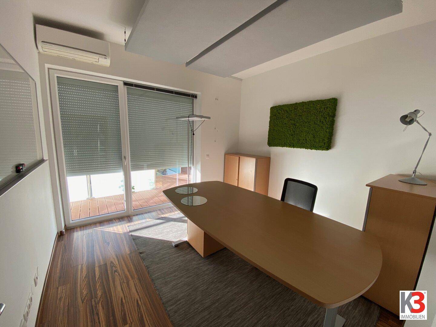 Helles Büro mit großem Schreibtisch, Bürostuhl und Fenster mit Jalousien.