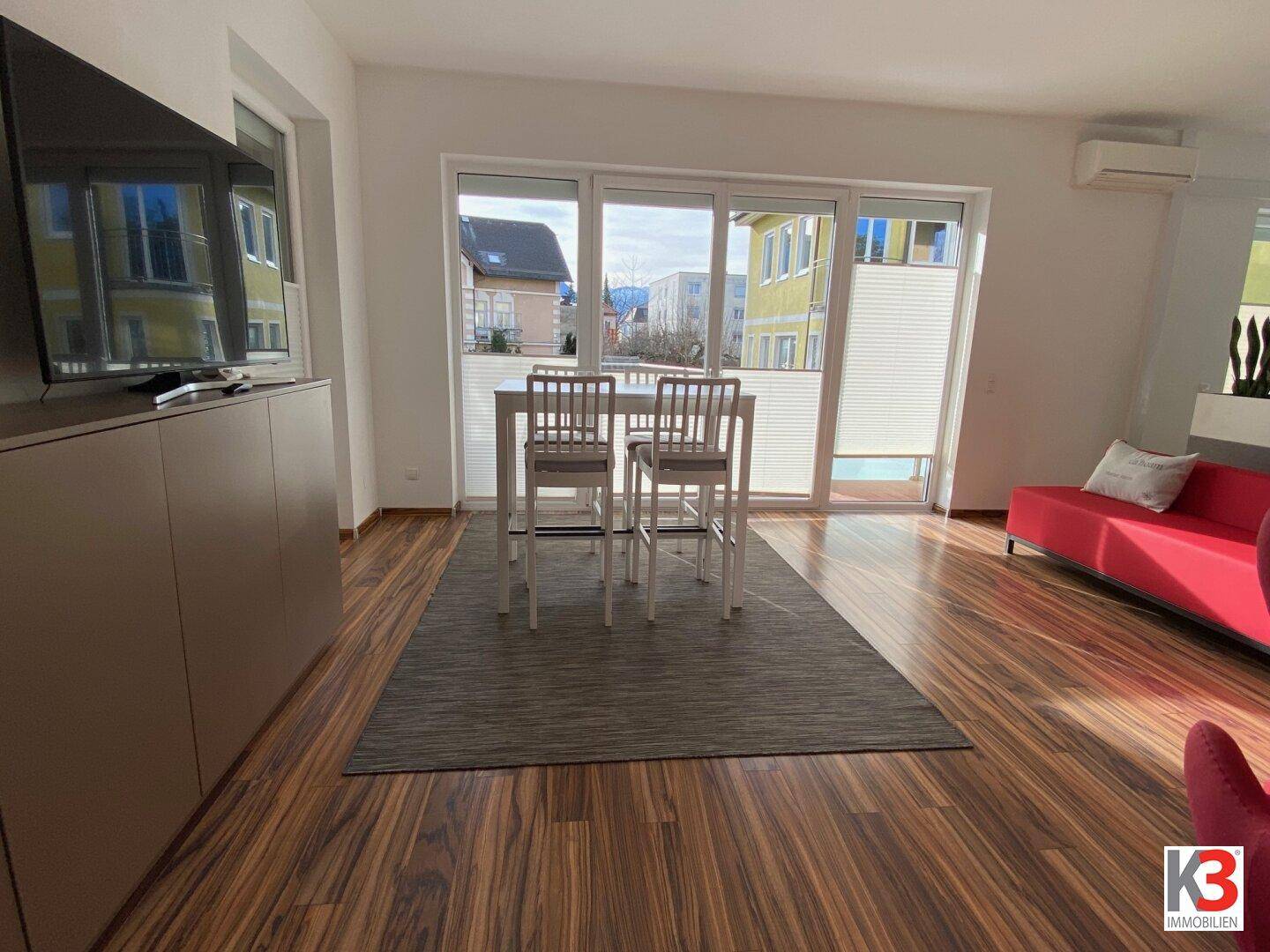 Heller Wohn- und Essbereich mit Holzboden, hohen Fenstern und Zugang zum Außenbereich.