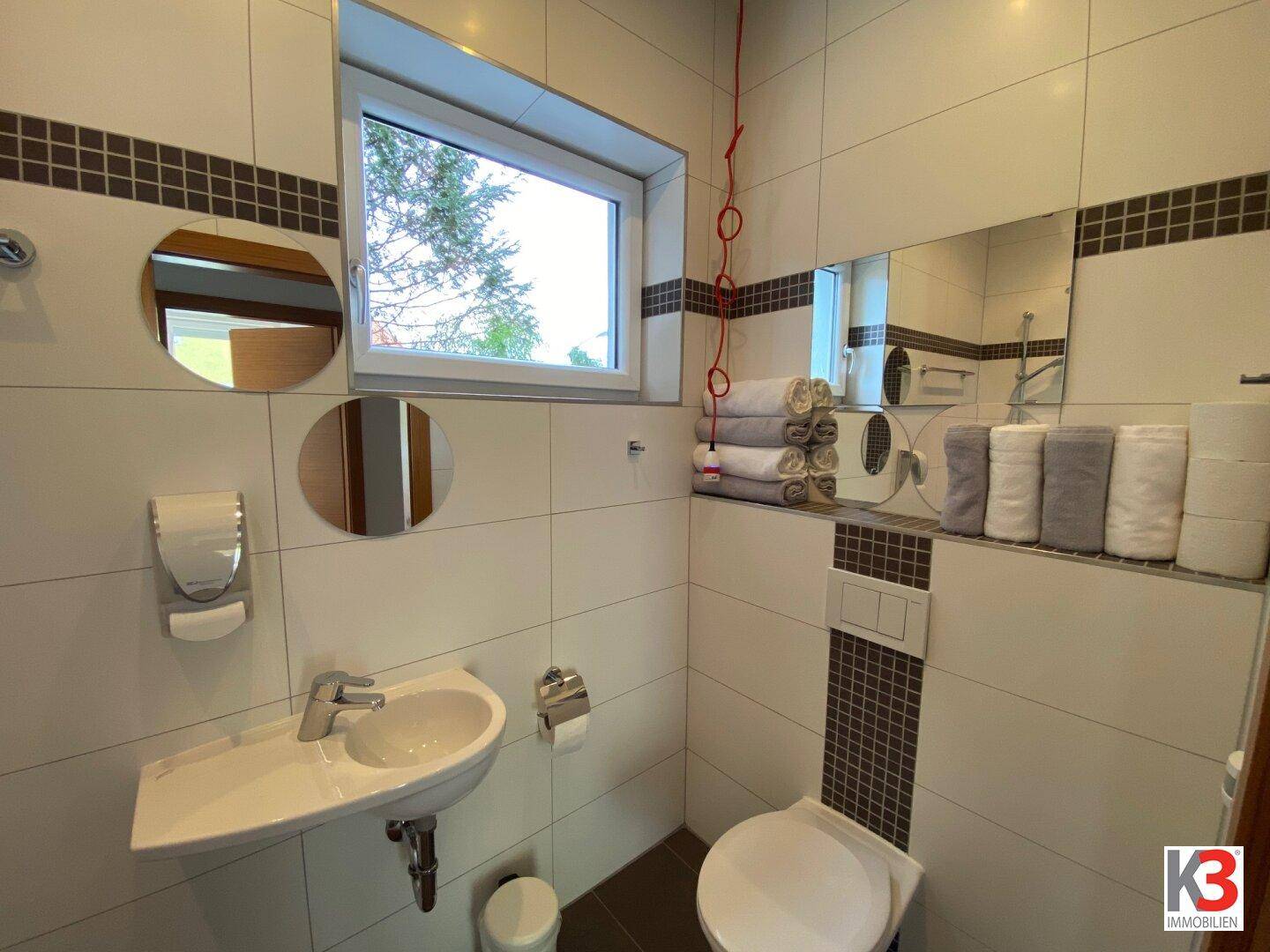 Helles Gäste-WC mit Waschbecken, Wandtoilette und Fenster für natürliche Belüftung.