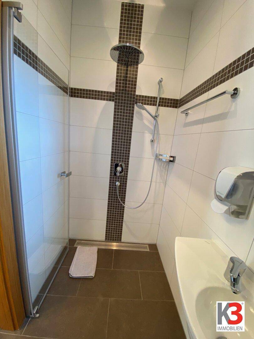 Moderne Duschkabine mit Regendusche und Handbrause, gefliest in Weiß und Dunkelbraun.