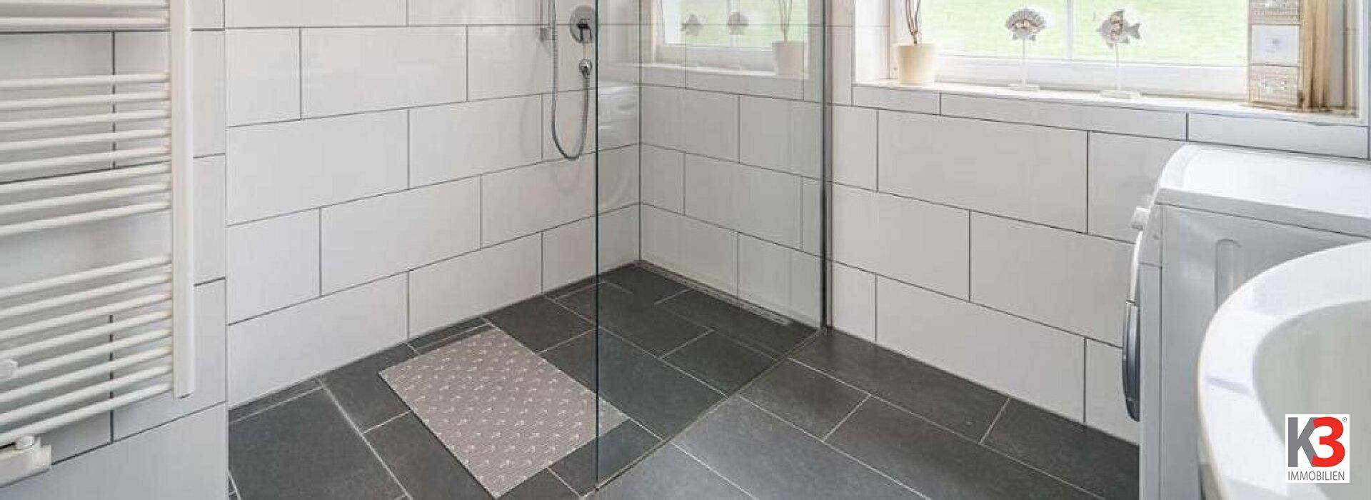 Modernes Badezimmer mit ebenerdiger Dusche, weißen Fliesen und Handtuchheizkörper.