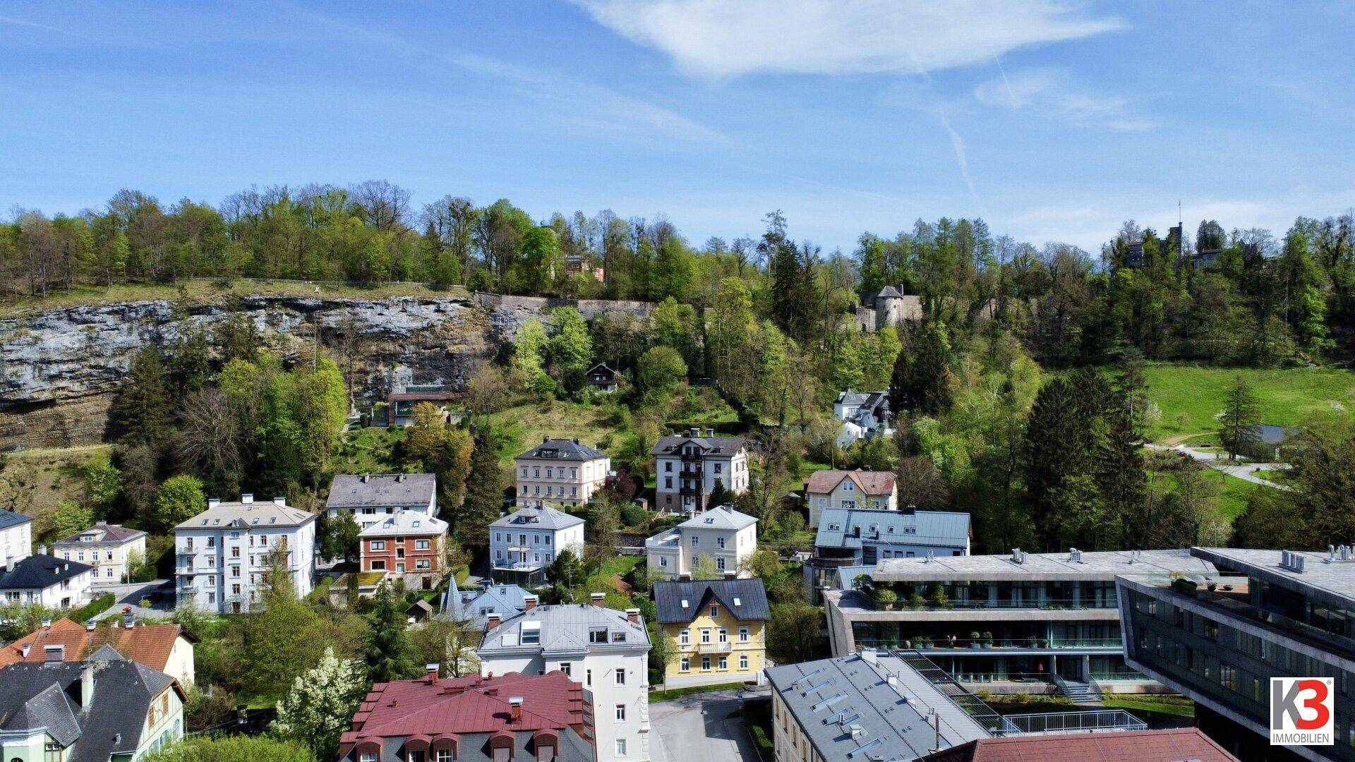 Blick auf eine Wohnsiedlung mit verschiedenen Häusern und bewaldeten Hügeln im Hintergrund.