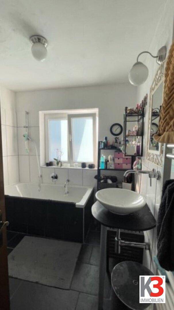 Badezimmer mit Badewanne, Einzelwaschbecken und Fenster, das natürliches Licht hereinlässt.