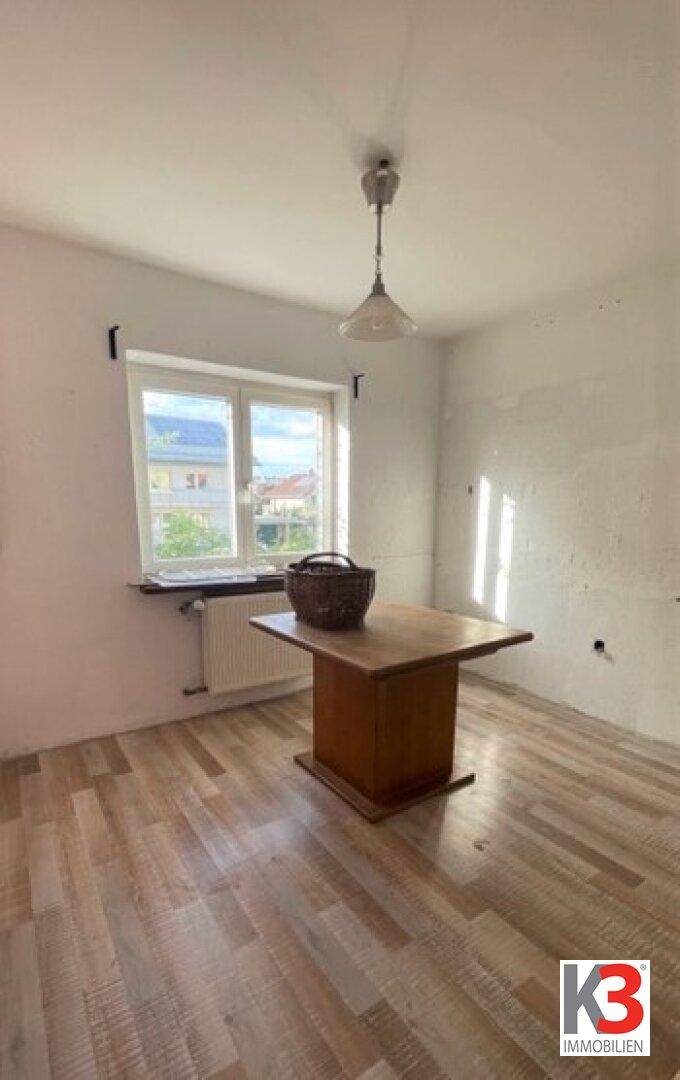 Leerer Raum mit Fenster und einem Holztisch, der auf eine Renovierung wartet.