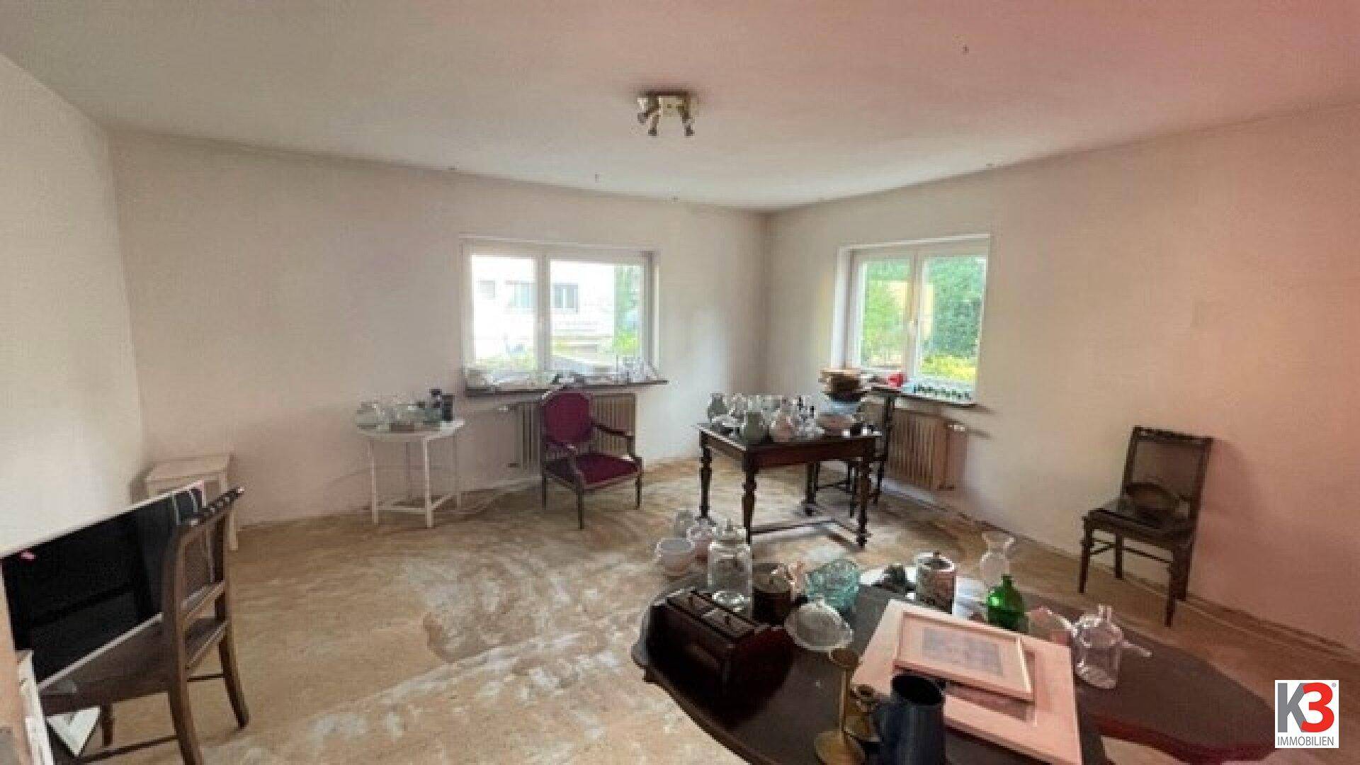 Geräumiges Wohnzimmer mit mehreren Fenstern und antiken Möbeln, das eine Renovierung benötigt.