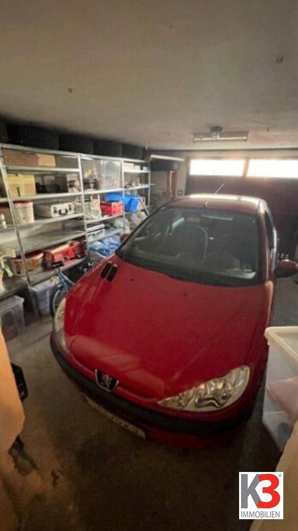 Rotes Auto parkt in einer Garage mit Regalen für Werkzeuge und Lagerung.