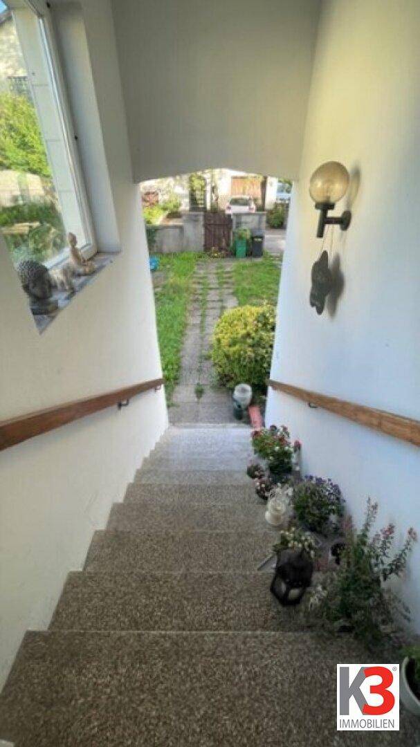 Außentreppe führt hinunter in einen grünen Gartenbereich mit Pflanzen am Wegesrand.