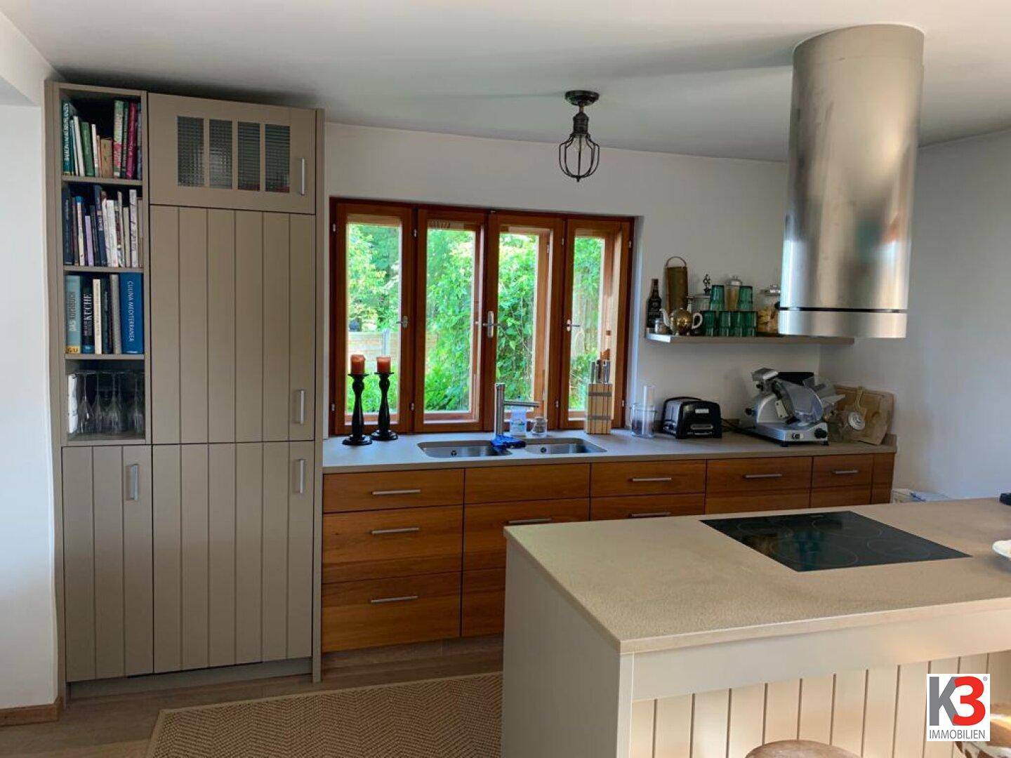 Moderne Küche mit Holzfronten, Spüle unter dem Fenster und großer Dunstabzugshaube.