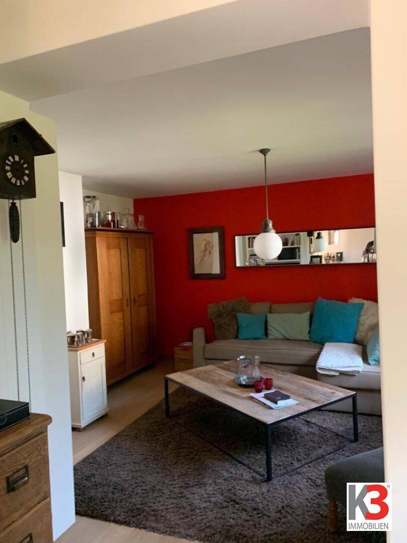 Gemütliches Wohnzimmer mit roter Akzentwand, beigem Sofa und Holztisch.