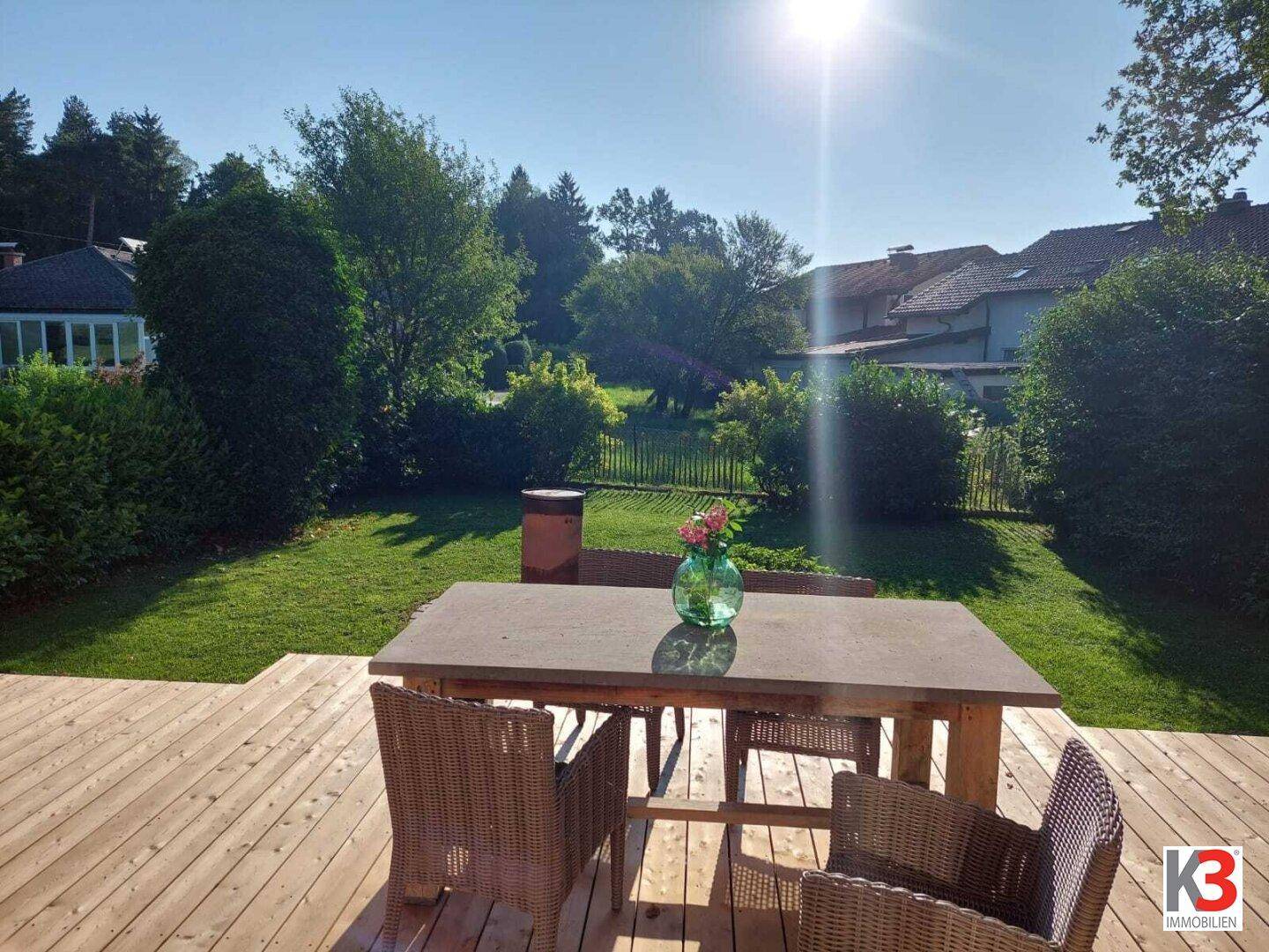Sonnige Holzterrasse mit Blick auf den weitläufigen Rasen und die umliegende Natur.