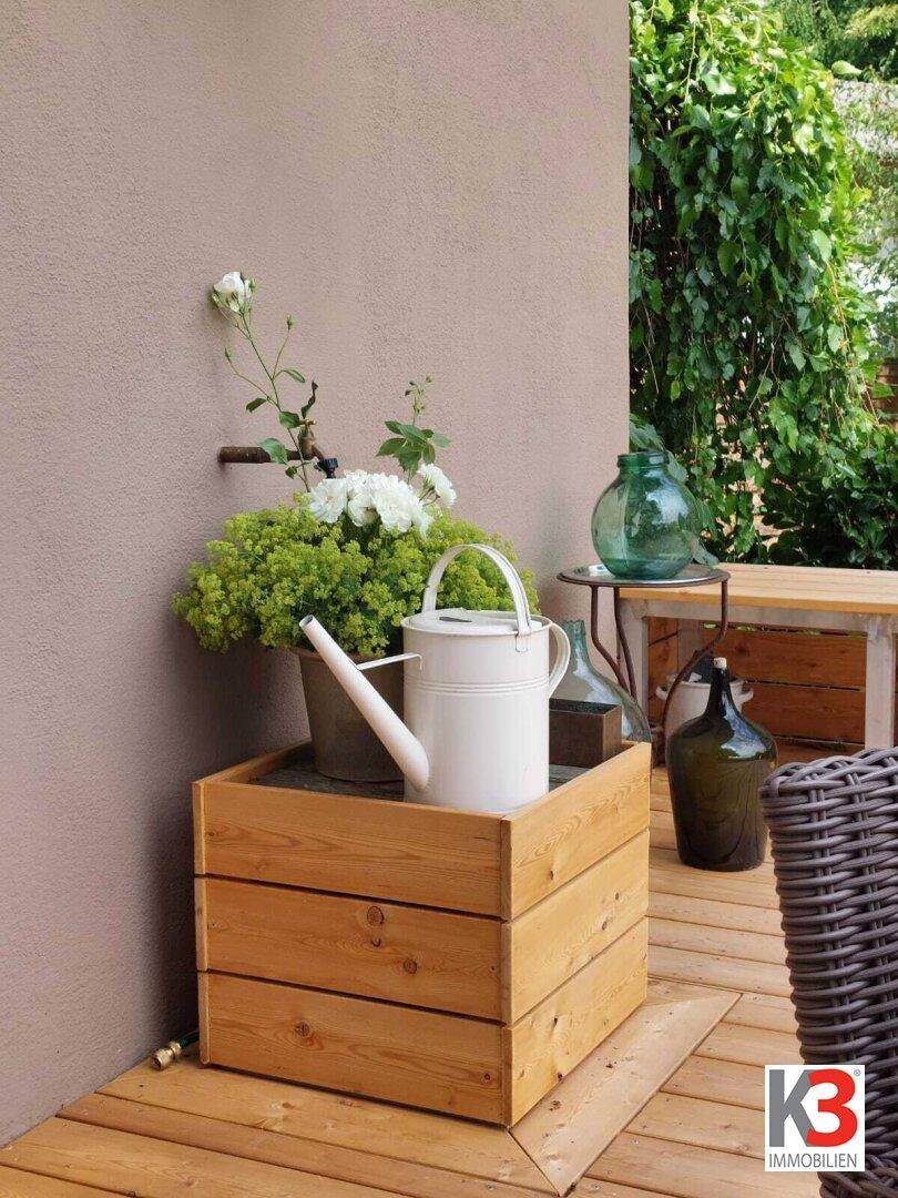Detailansicht der Holzterrasse mit Pflanzen, Gießkanne und rustikalen Dekorationen.