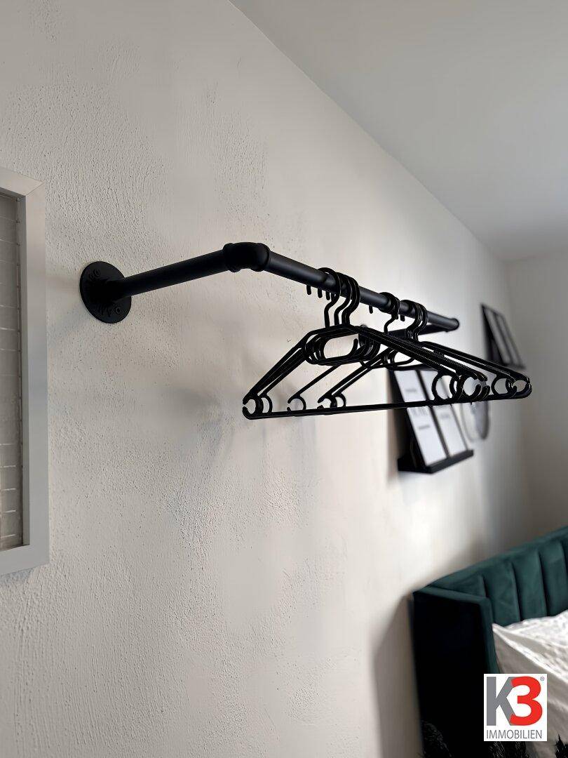 Industrieller Kleiderständer aus schwarzem Metall mit Kleiderbügeln an einer weißen Wand.