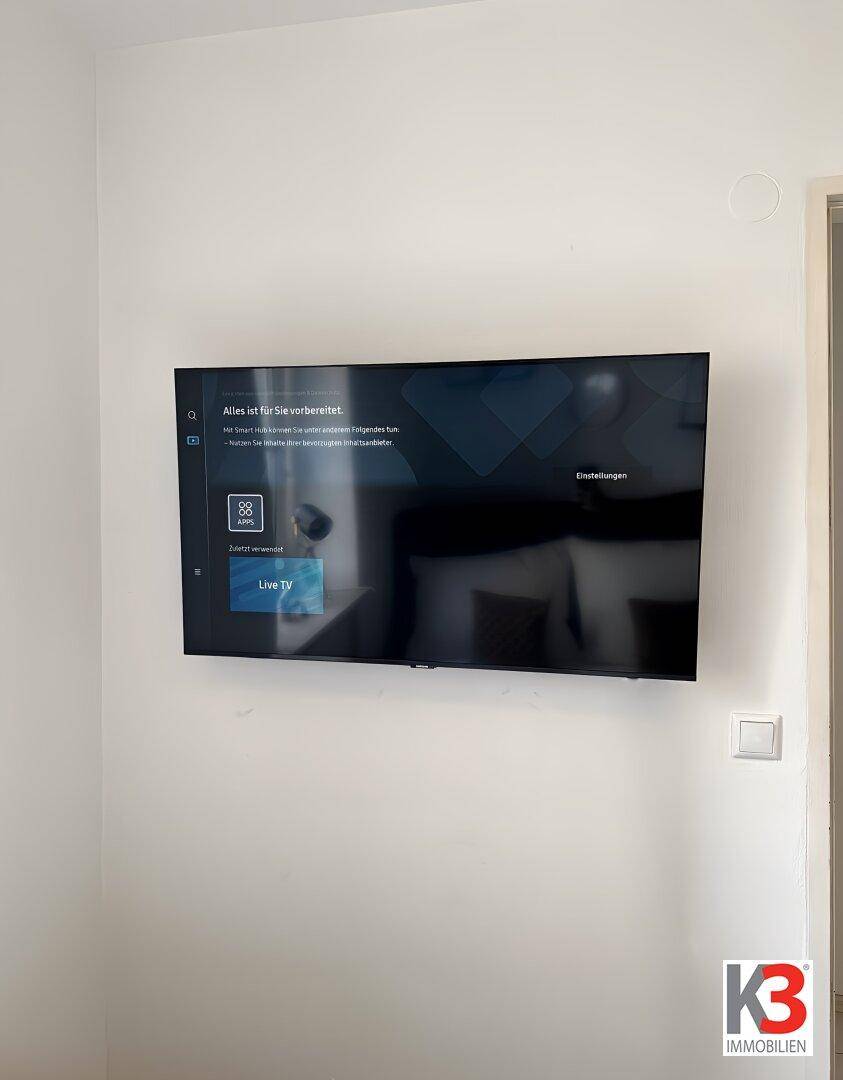 Wandmontierter Flachbildfernseher an einer schlichten weißen Wand.