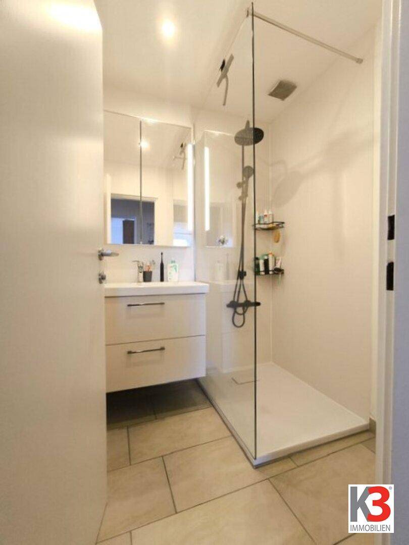 Modernes Badezimmer mit ebenerdiger Dusche, Glasabtrennung und Waschtisch mit Spiegelschrank.