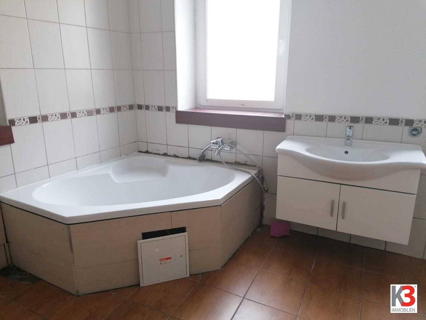 Badezimmer mit Eckbadewanne, Einzelwaschbecken und Fenster für natürliches Licht.