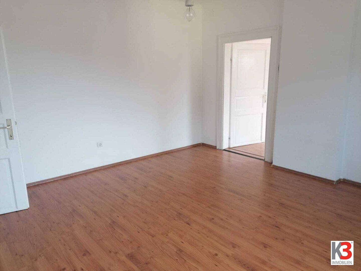 Leeres Zimmer mit Holzboden und weiß gestrichenen Wänden, bereit zur individuellen Gestaltung.