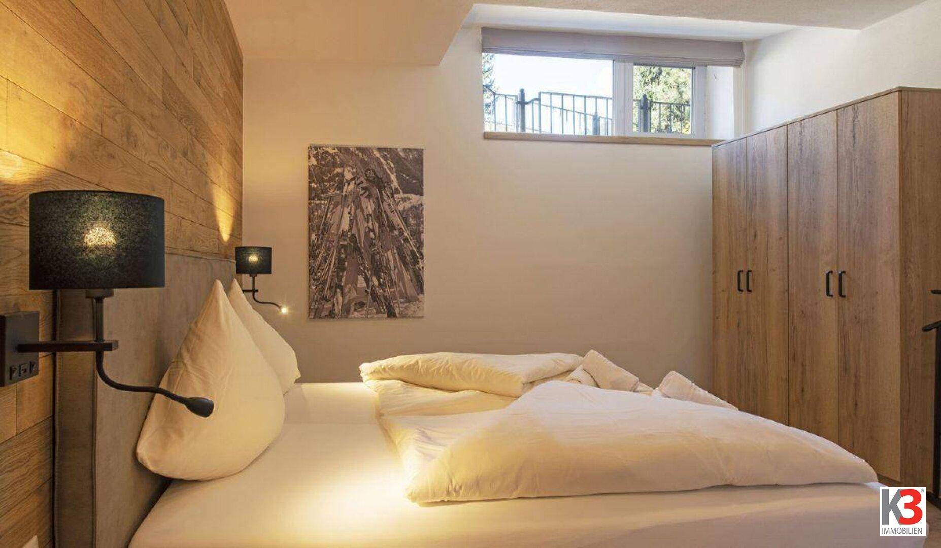 Gemütliches Schlafzimmer mit Holzwand, Doppelbett und Fenster mit Blick ins Grüne.