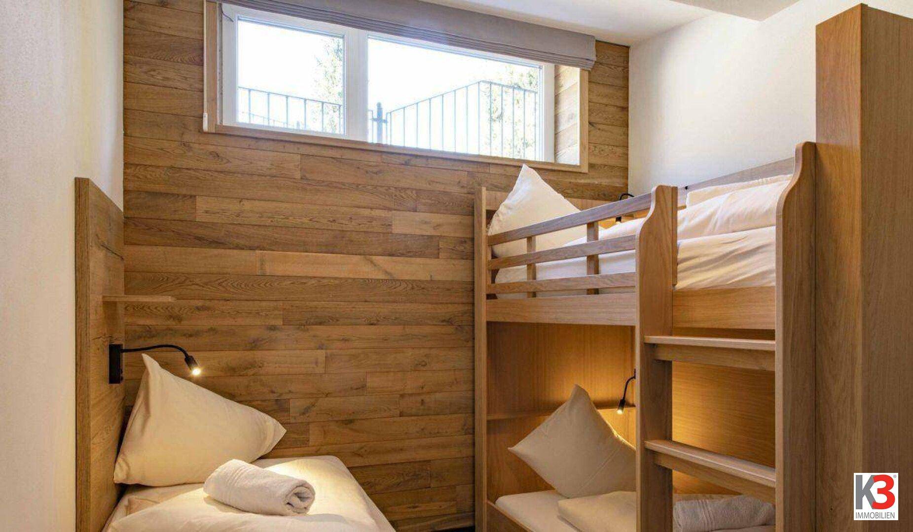 Kinderzimmer mit Etagenbett, Einzelbett und Holzwandverkleidung.